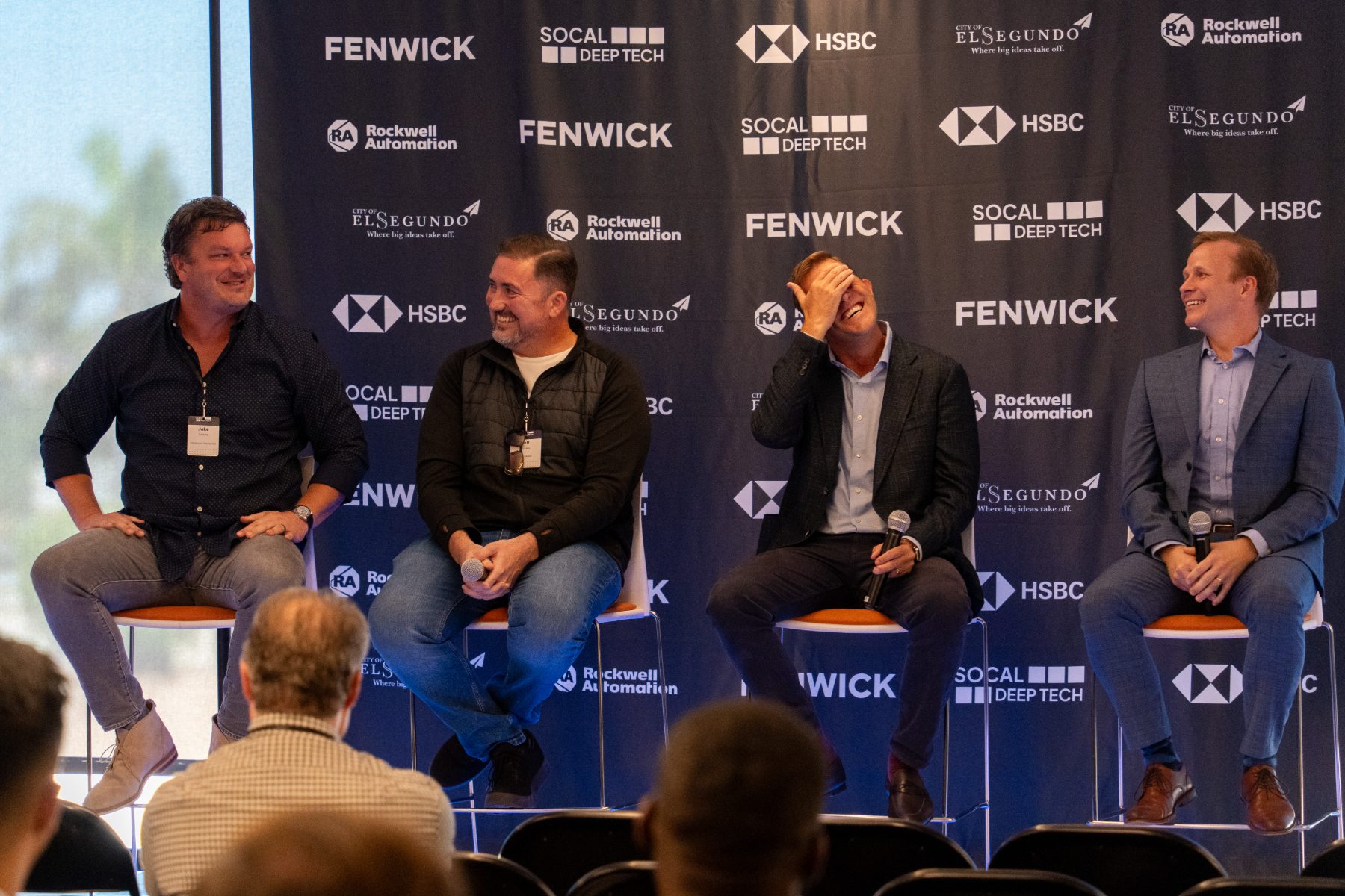 Four panelists on stools in front of a sponsor backdrop